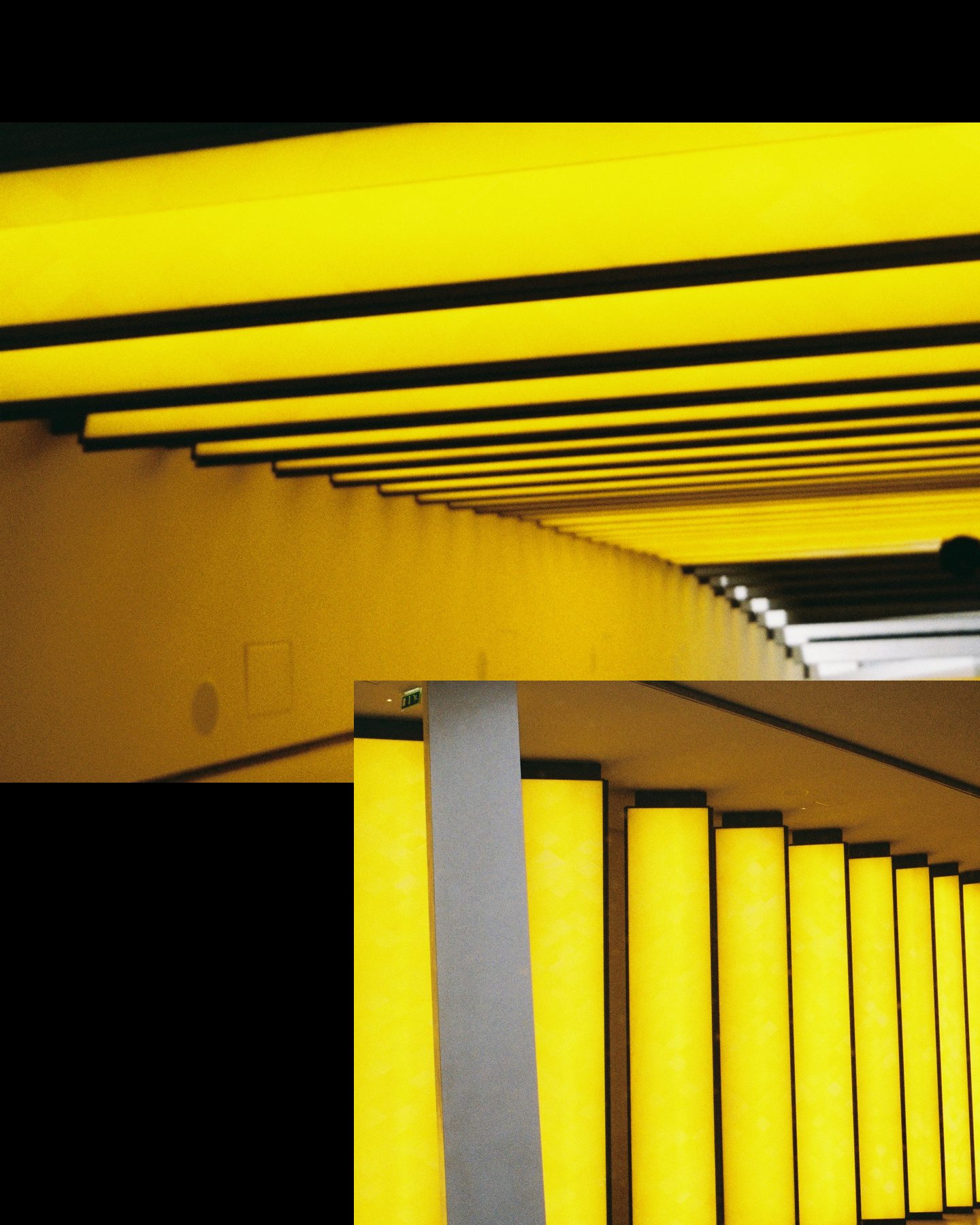 Slide 1 of 2: a corridor ceiling of yellow light bars and a row of glowing yellow columns